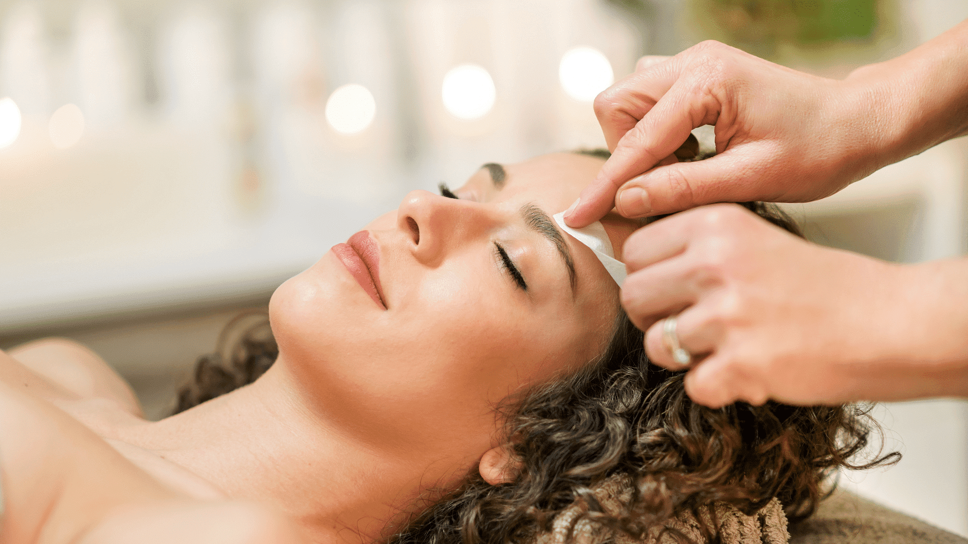 Woman receiving eyebrow waxing treatment in spa setting.